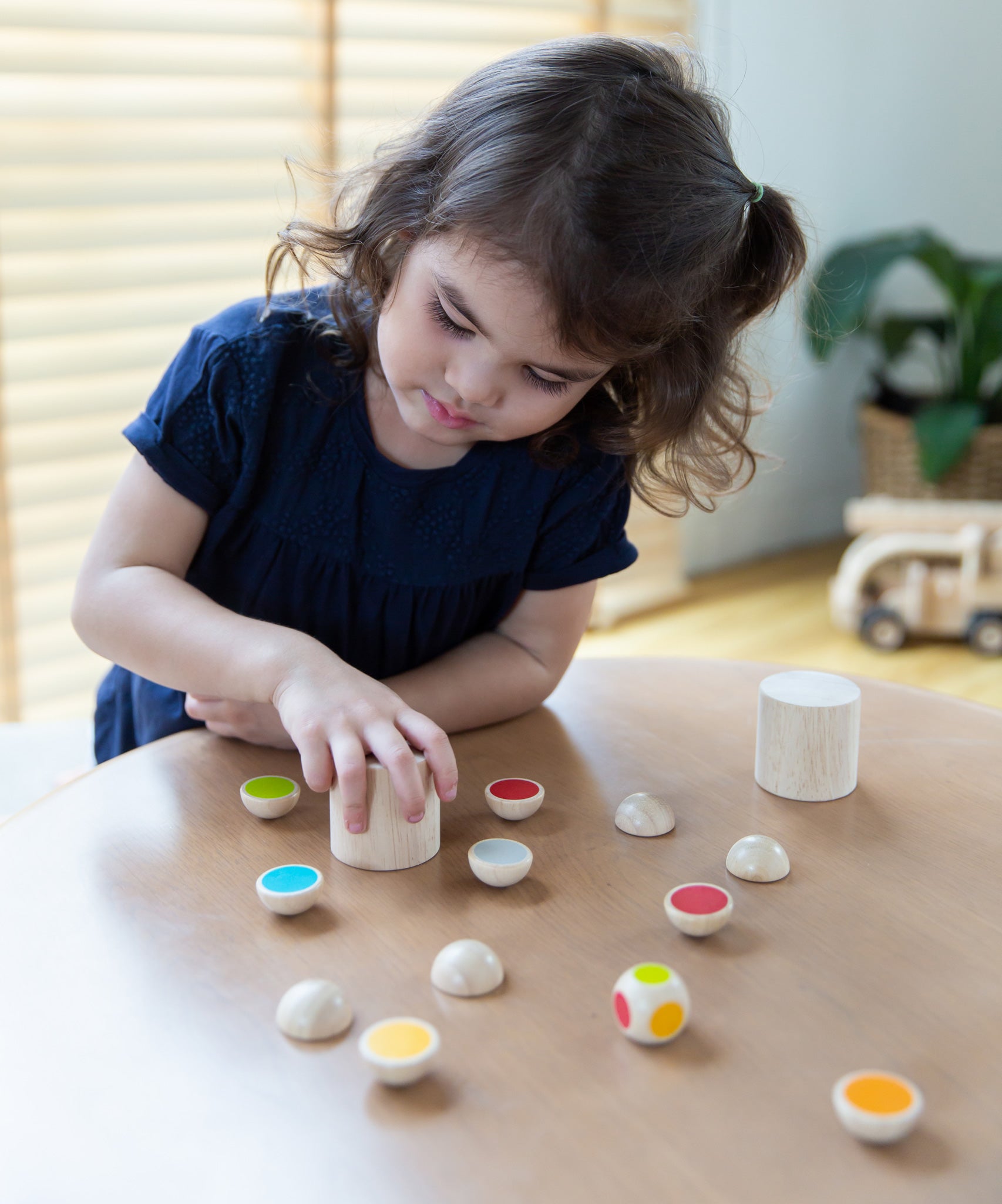 A child sitting by the table playing with the PlanToys Wooden shake and flip game.