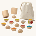 PlanToys Wooden shake and flip game pictured on a plain background. The pieces of the game are next to a small canvas storage bag. 