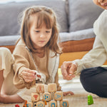 A child and adult sitting on a rug playing with the PlanToys Storytelling Dice Set.