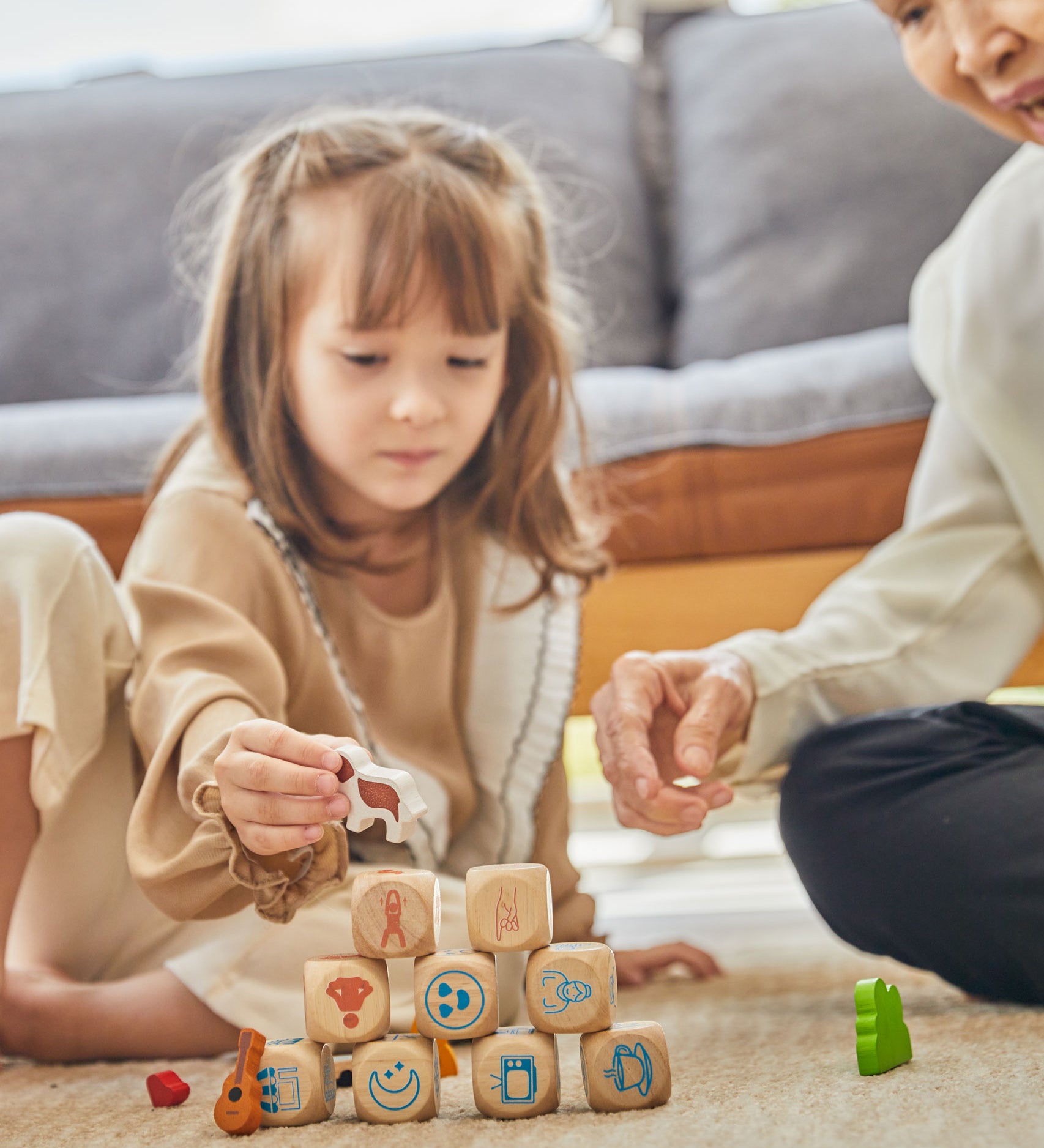 A child and adult sitting on a rug playing with the PlanToys Storytelling Dice Set.