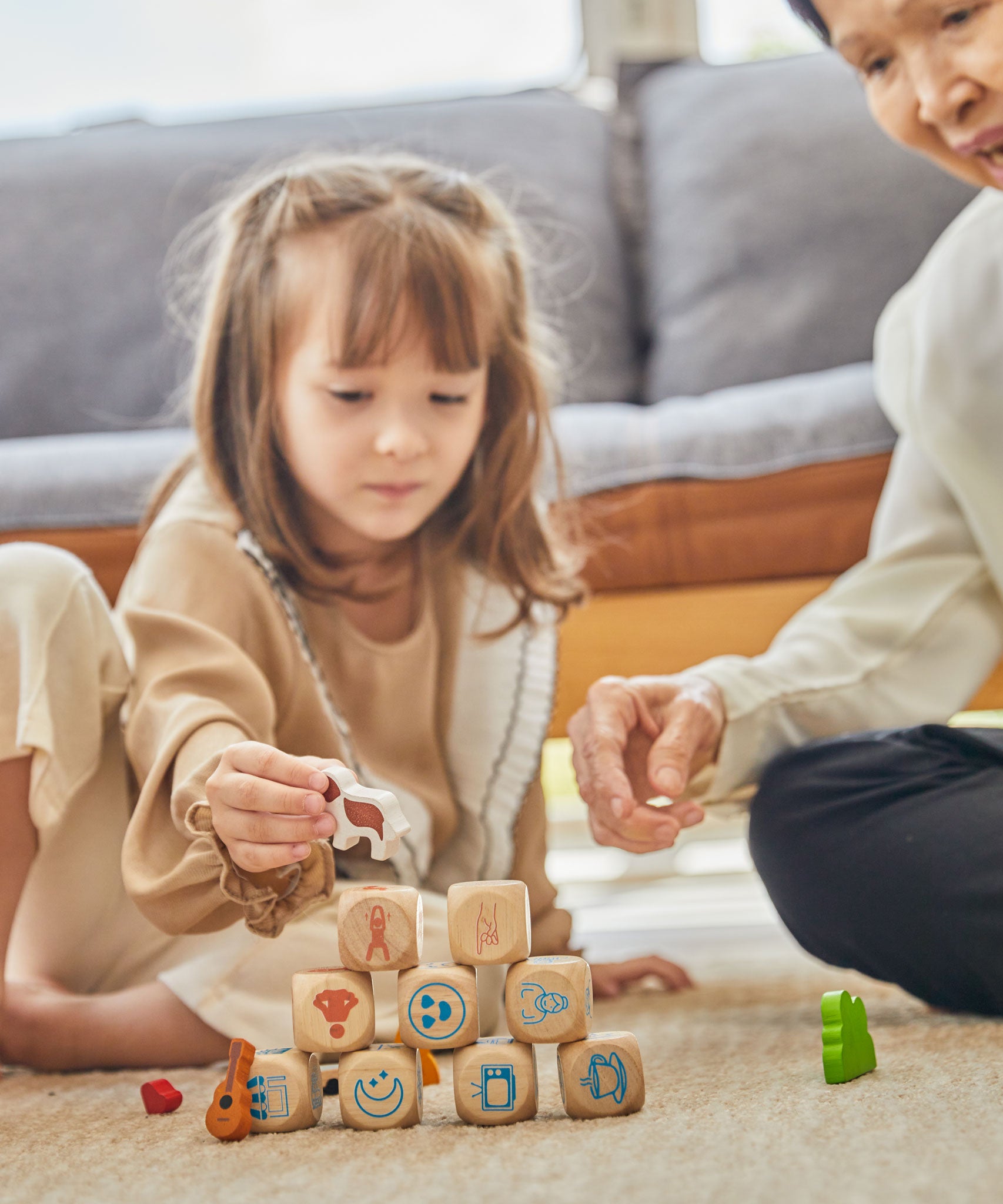 A child and adult sitting on a rug playing with the PlanToys Storytelling Dice Set.