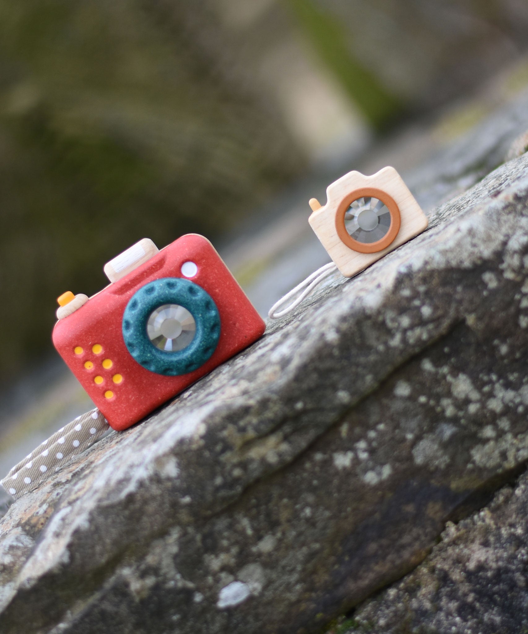 The PlanToys My First Camera pictured next to the mini PlanToys camera on a stone step outdoors. 