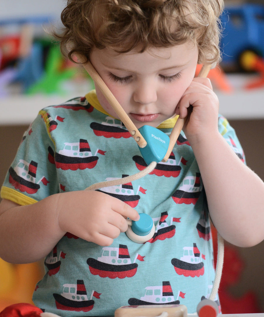 A child playing with the PlanToys Doctor Set, they have the stethoscope on and they are listing to their own heart.