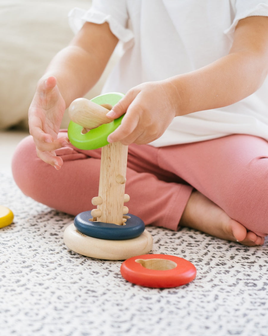 Close up of child's hands sliding green disc onto the PlanToys twist and sort game