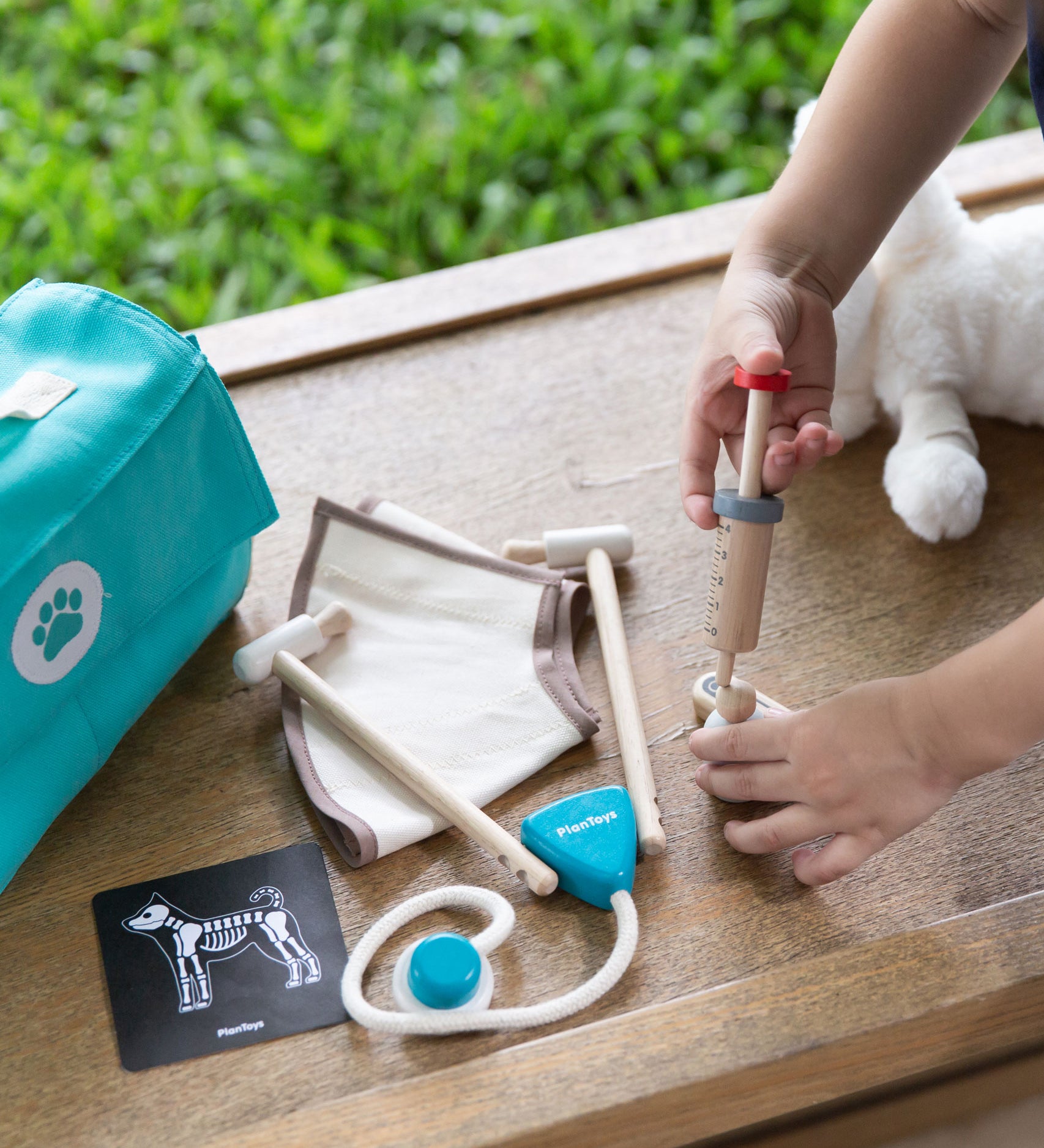 A close up of a child's hand playing with the Plan Toys Play Vet Set. 