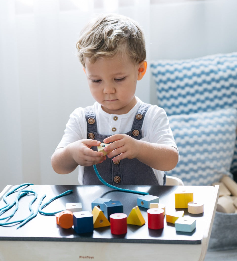 Child sat at a table threading plastic-free lacing blocks onto a blue string