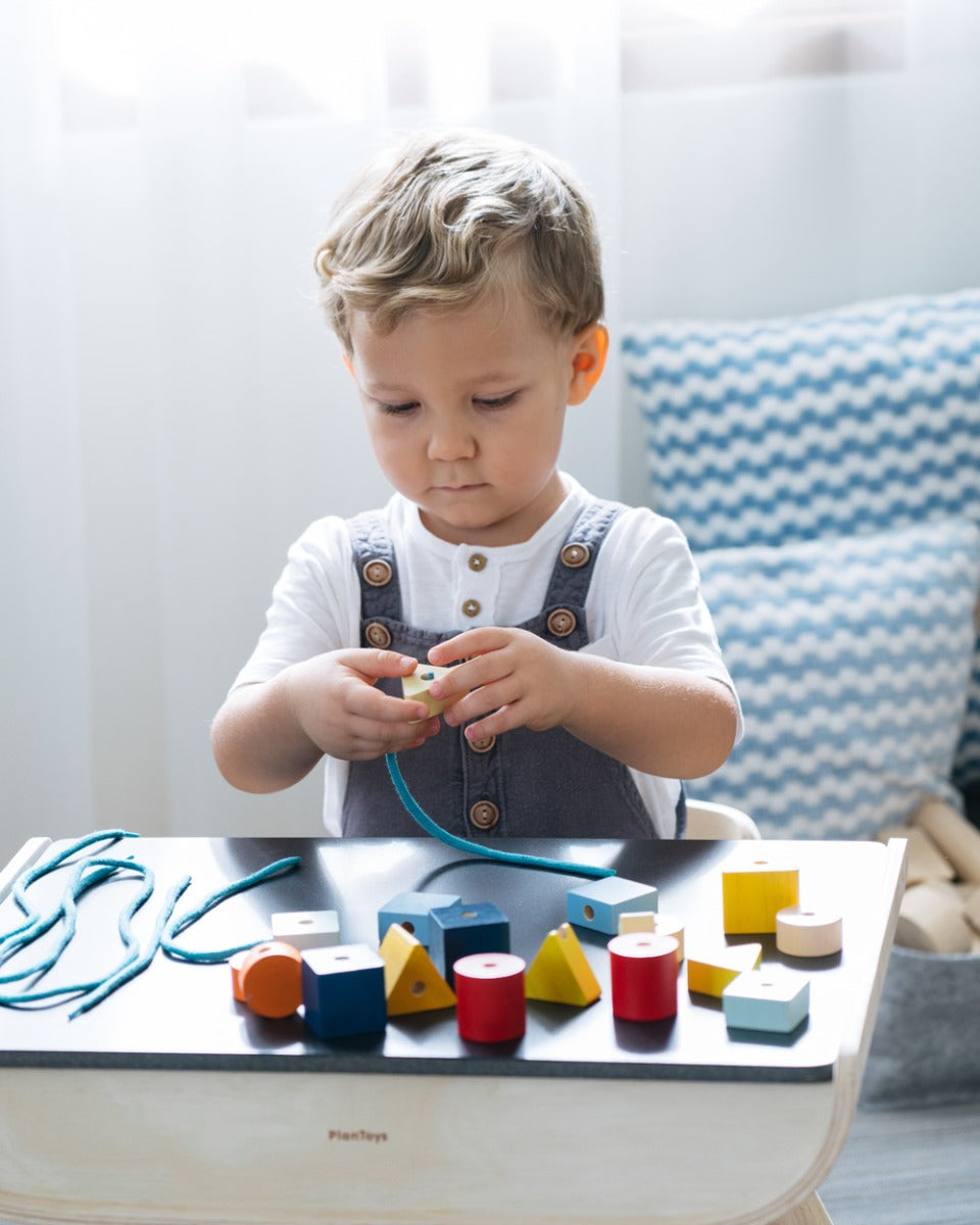 Child sat at a table threading plastic-free lacing blocks onto a blue string