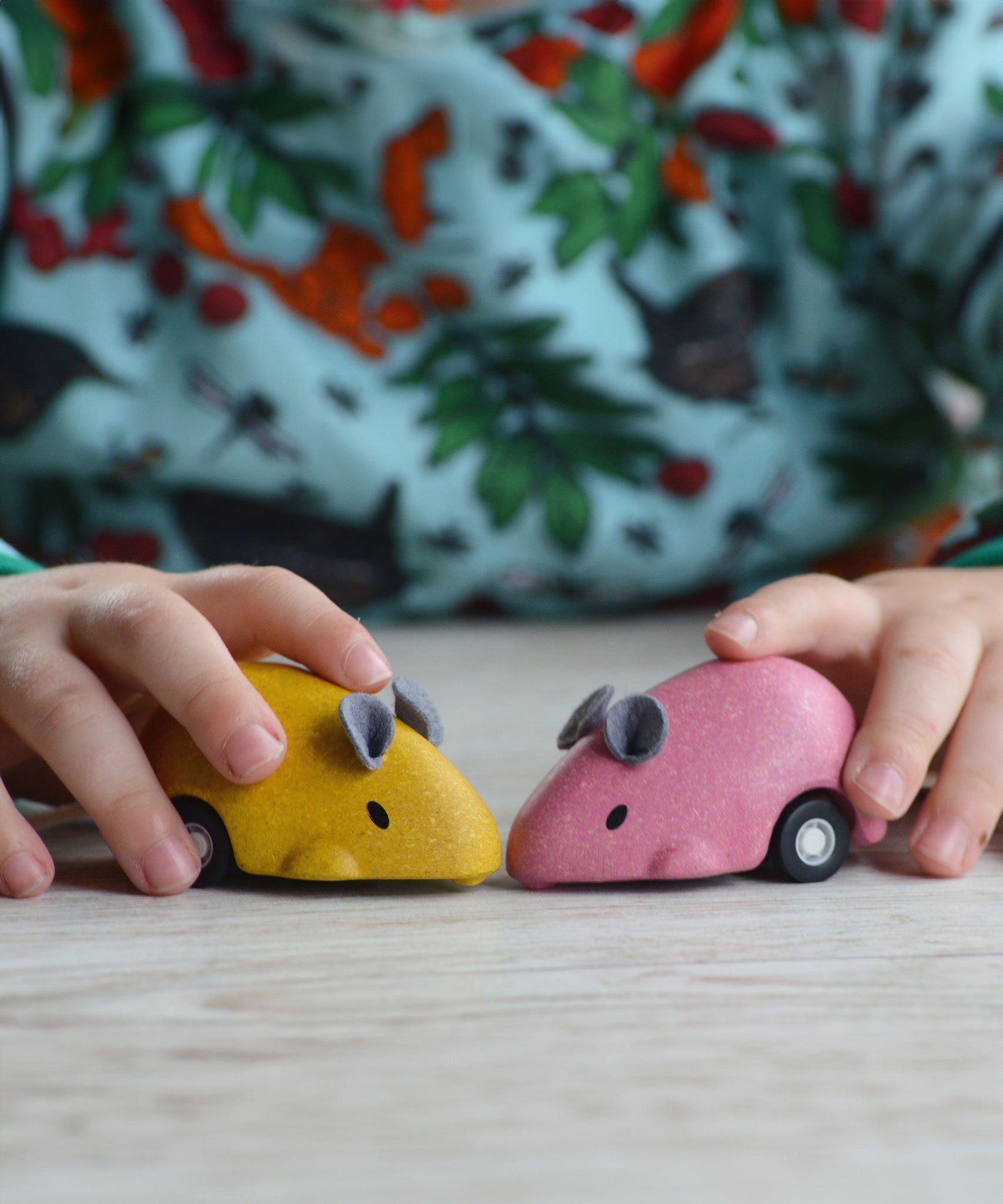 A close up of the PlanToys Wooden Pull-Back Mouse Toys in yellow and pink in a child's hands.