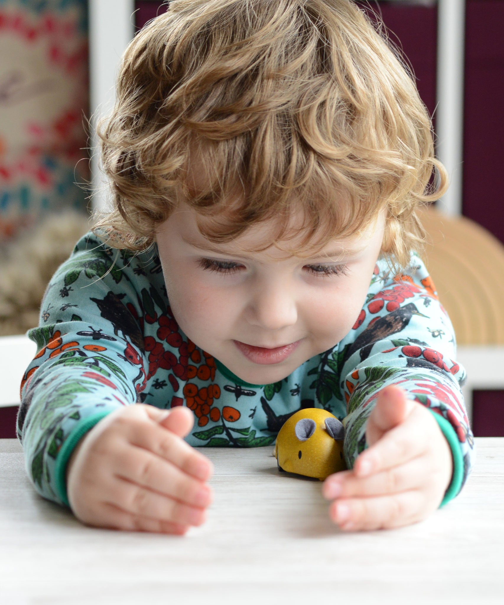 A child playing with a yellow PlanToys Wooden Pull-Back Mouse.