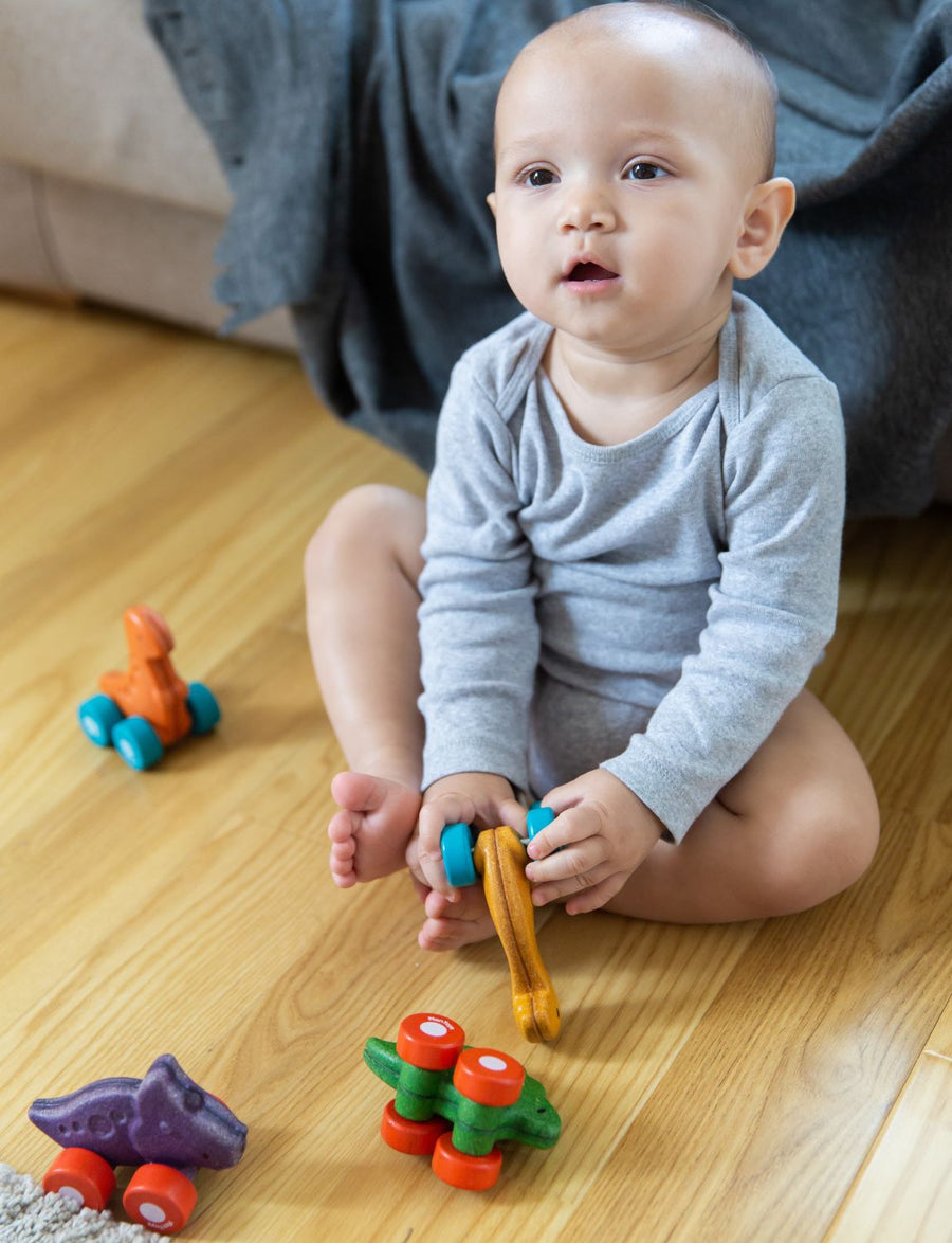 Toddler playing with four PlanToys Dino Cars on a wooden floor