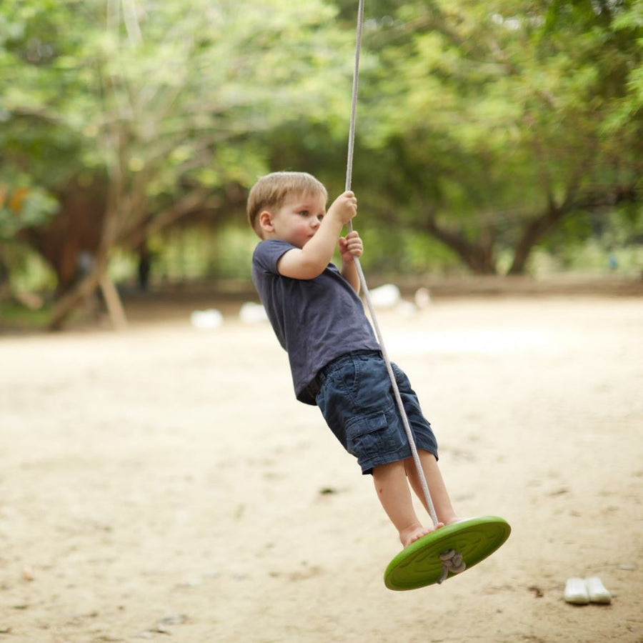 Child swinging standing up outside on the PlanToys Saucer Disc Swing