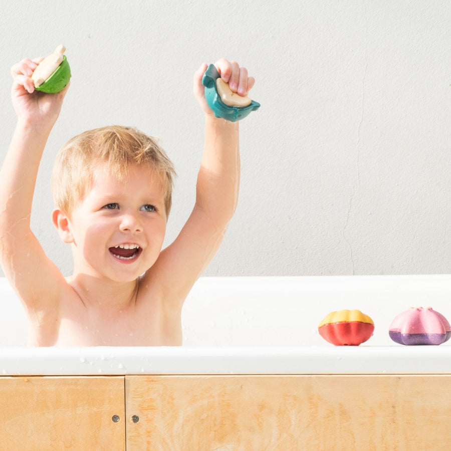 Child playing with the PlanToys Sea Life Bath Set in the bath with the Shell bath toy on the side of the bath.