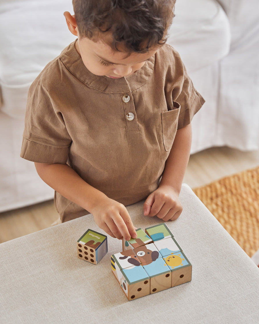 Close up of boy stacking the Waldorf PlanToys animal puzzle toy blocks on a beige cushion