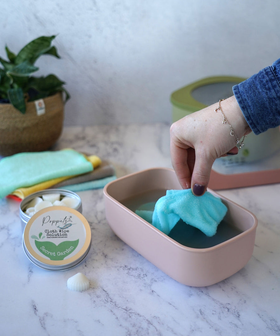 An adult's hand reaching for a wipe from the pink coloured Poppets reusable wipes container. 