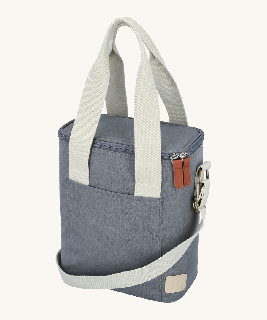 The Lola & Lykke Milk Cooler Bag on a cream background. The bag is denim blue in colour with white carry straps and shoulder strap