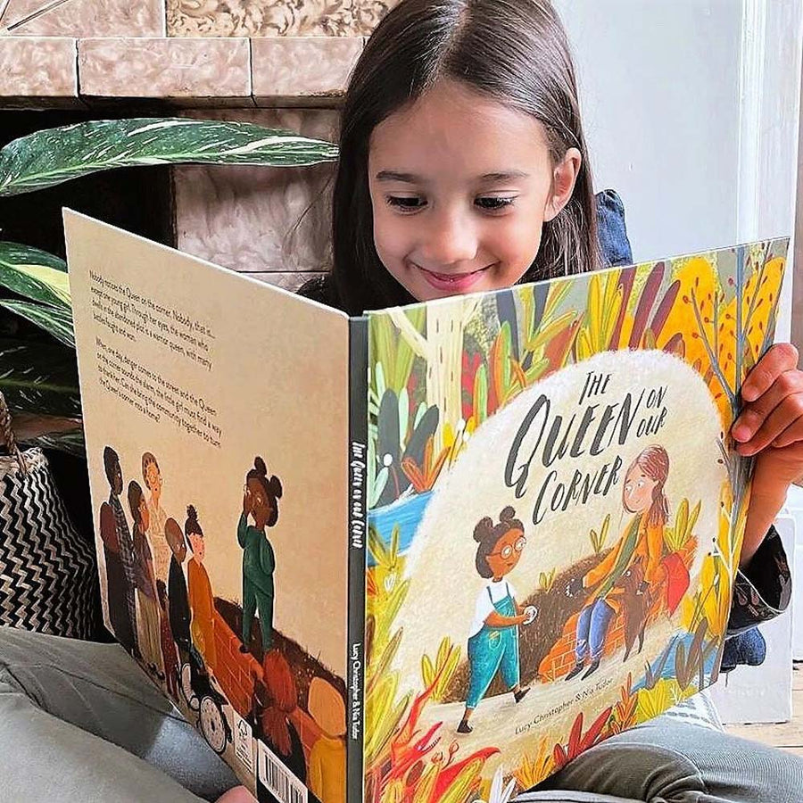 Girl sat cross legged reading the Queen on our Corner childrens story book