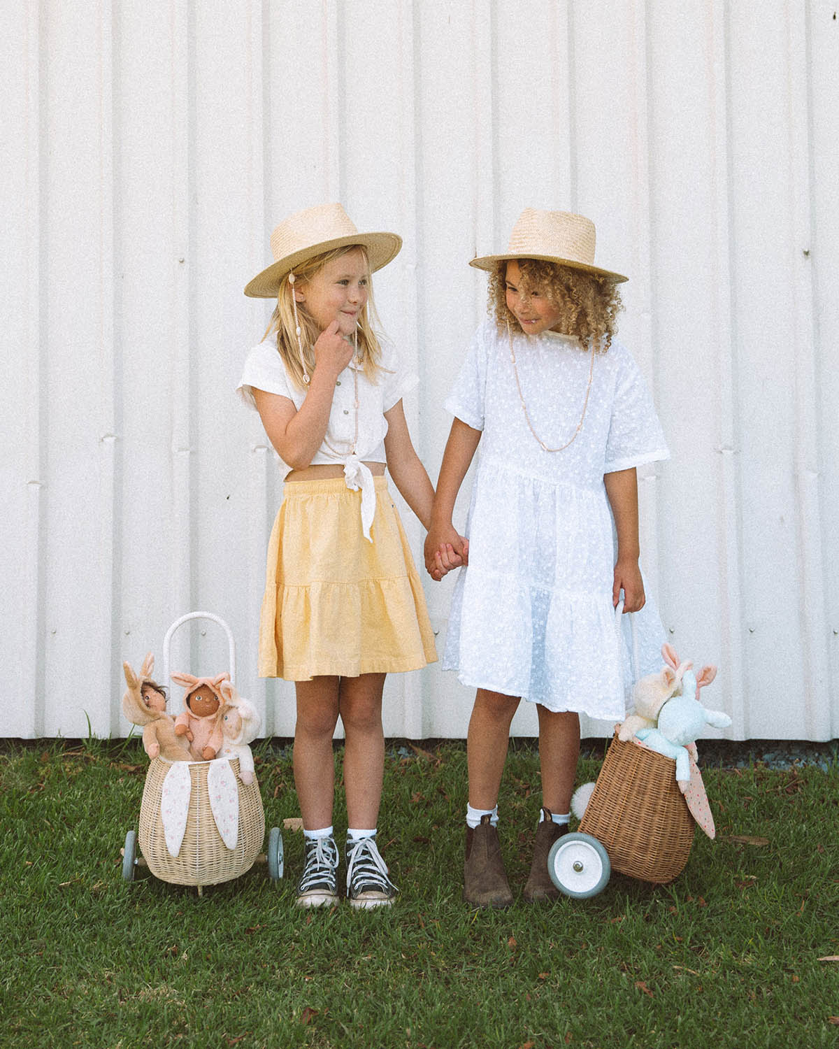 stood next to a fence outside. The child is holding the handle of the Olli Ella Rattan Bunny Luggy with Lining – Pansy Floral. A beautifully woven pull along Luggy basket with cream cotton lining with a vintage pa