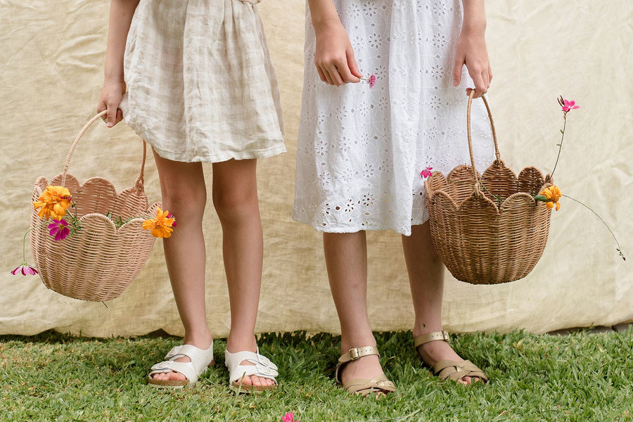 The Olli Ella Rattan Tulip Carry Basket - Natural holding a dozy Dinkum on a baby changing table