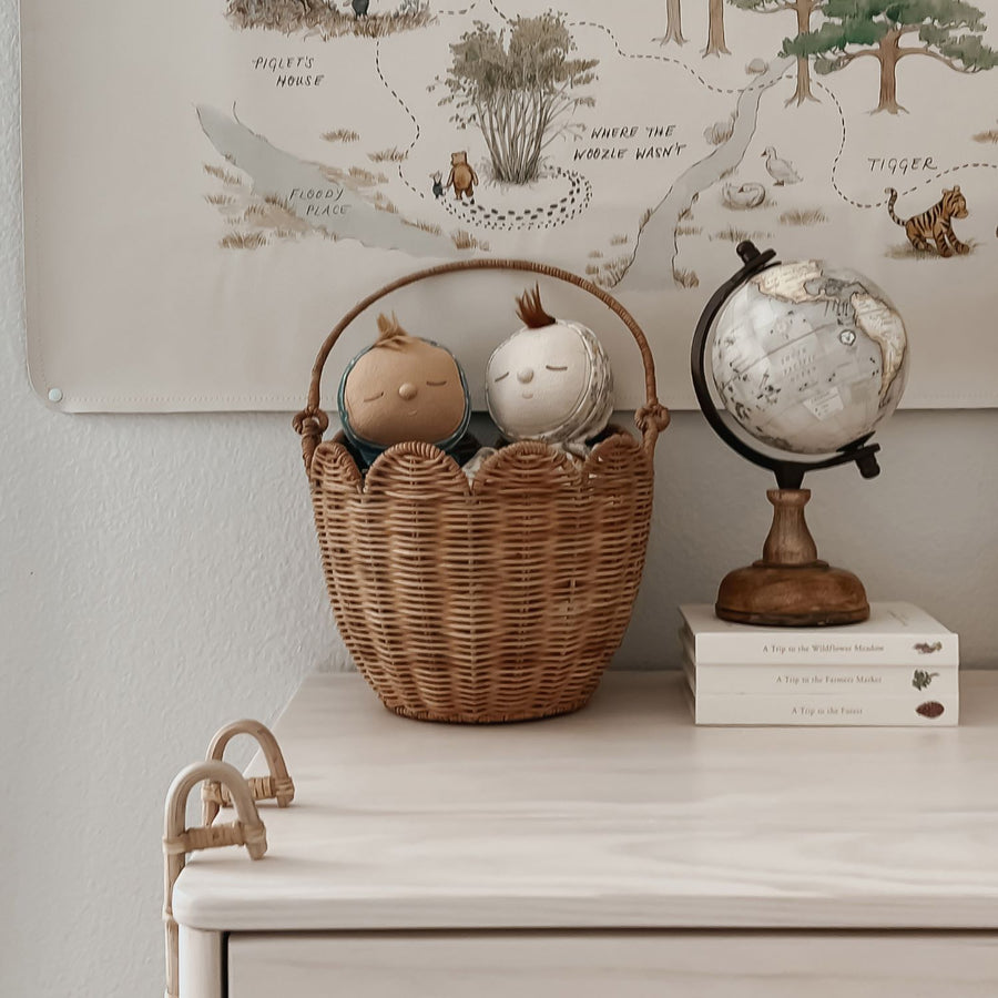 The Olli Ella Rattan Tulip Carry Basket - Natural holding two Dozy Dinkums on a chest of draws next to a globe