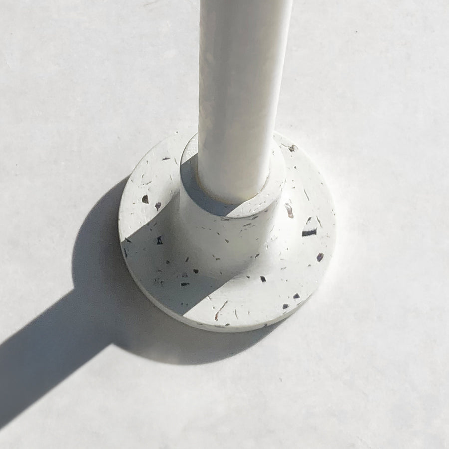 Rawr Shell Terrazzo Candlestick on a concrete surface. The candlestick has a white candle inserted into it.