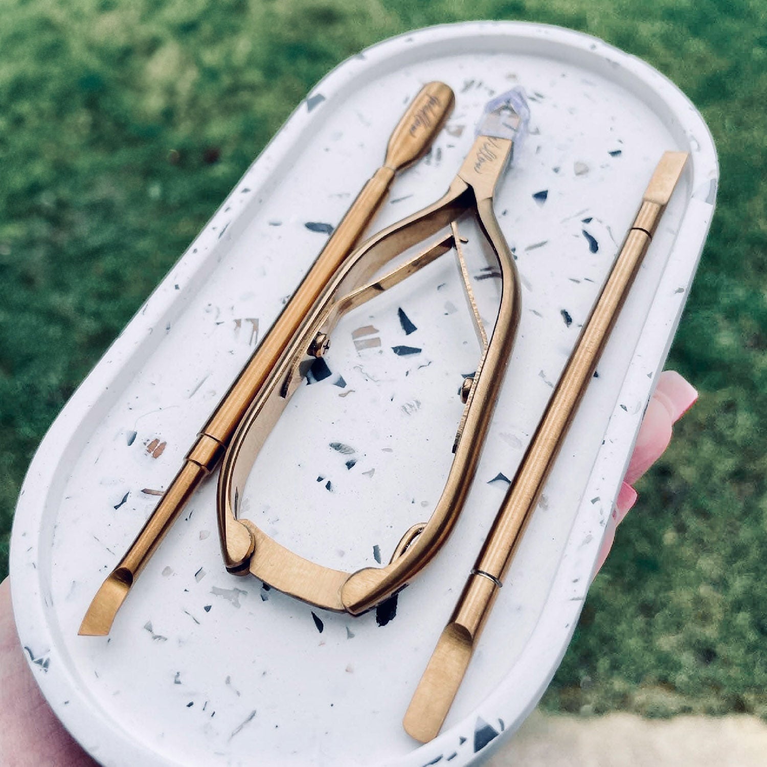 Rawr Shell Terrazzo Oval Tray held aloft by an adult hand in an outdoor environment. The tray has manicure tools within it.