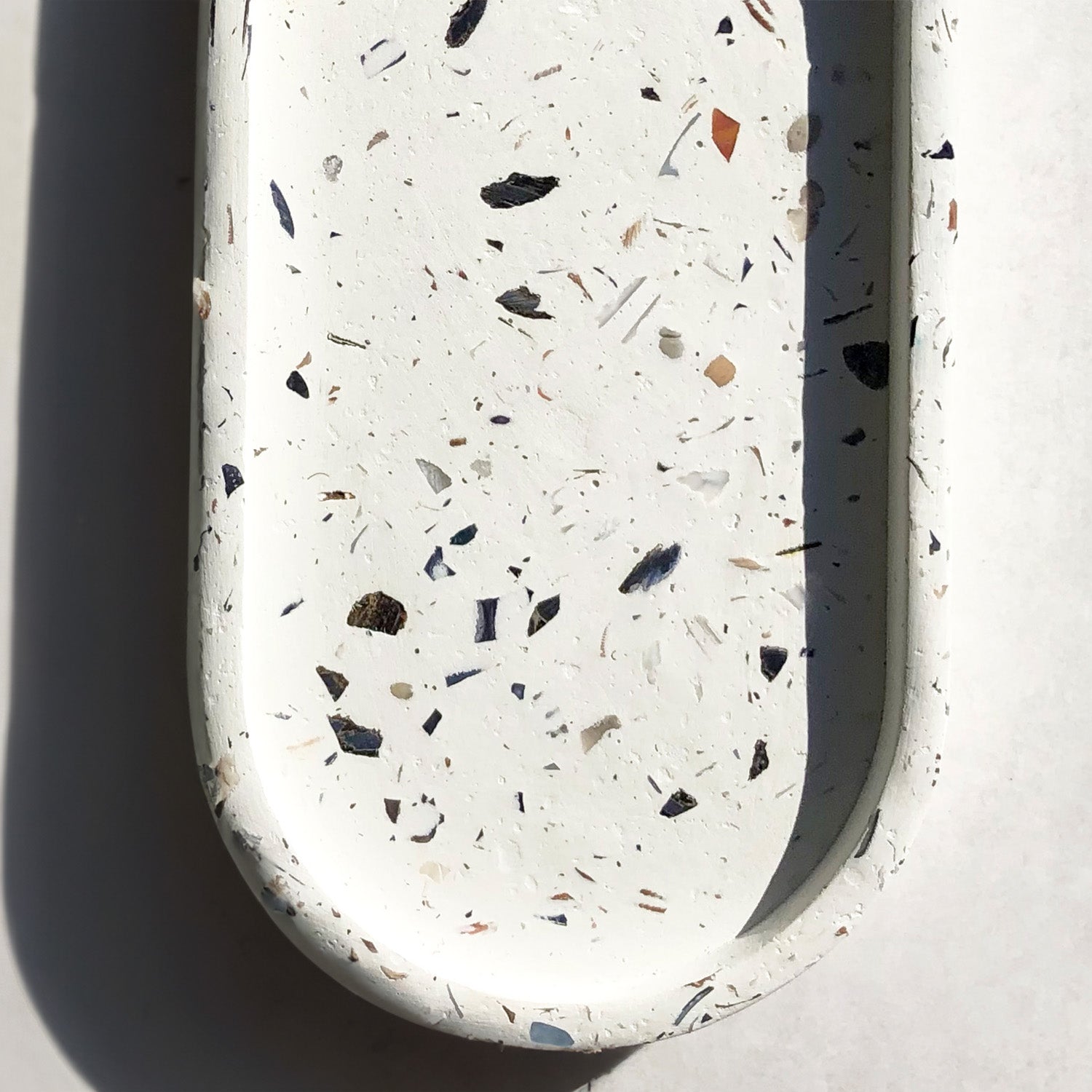 Rawr Shell Terrazzo Oval Tray on a concrete background. Three-quarters of the tray is showing