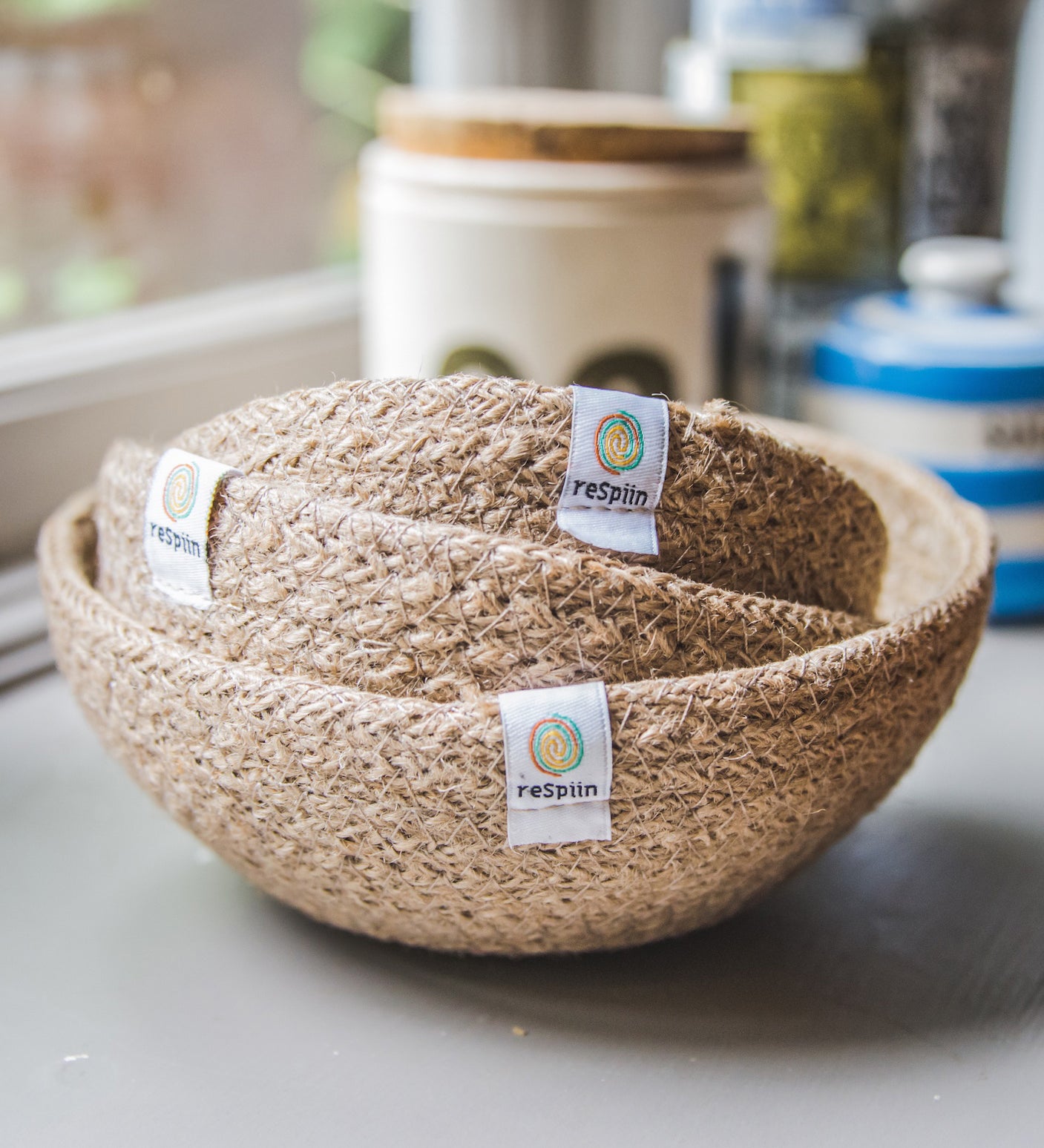 A set of three natural ReSpiin Jute Mini Bowl Set shown nestled inside each other on a window sill