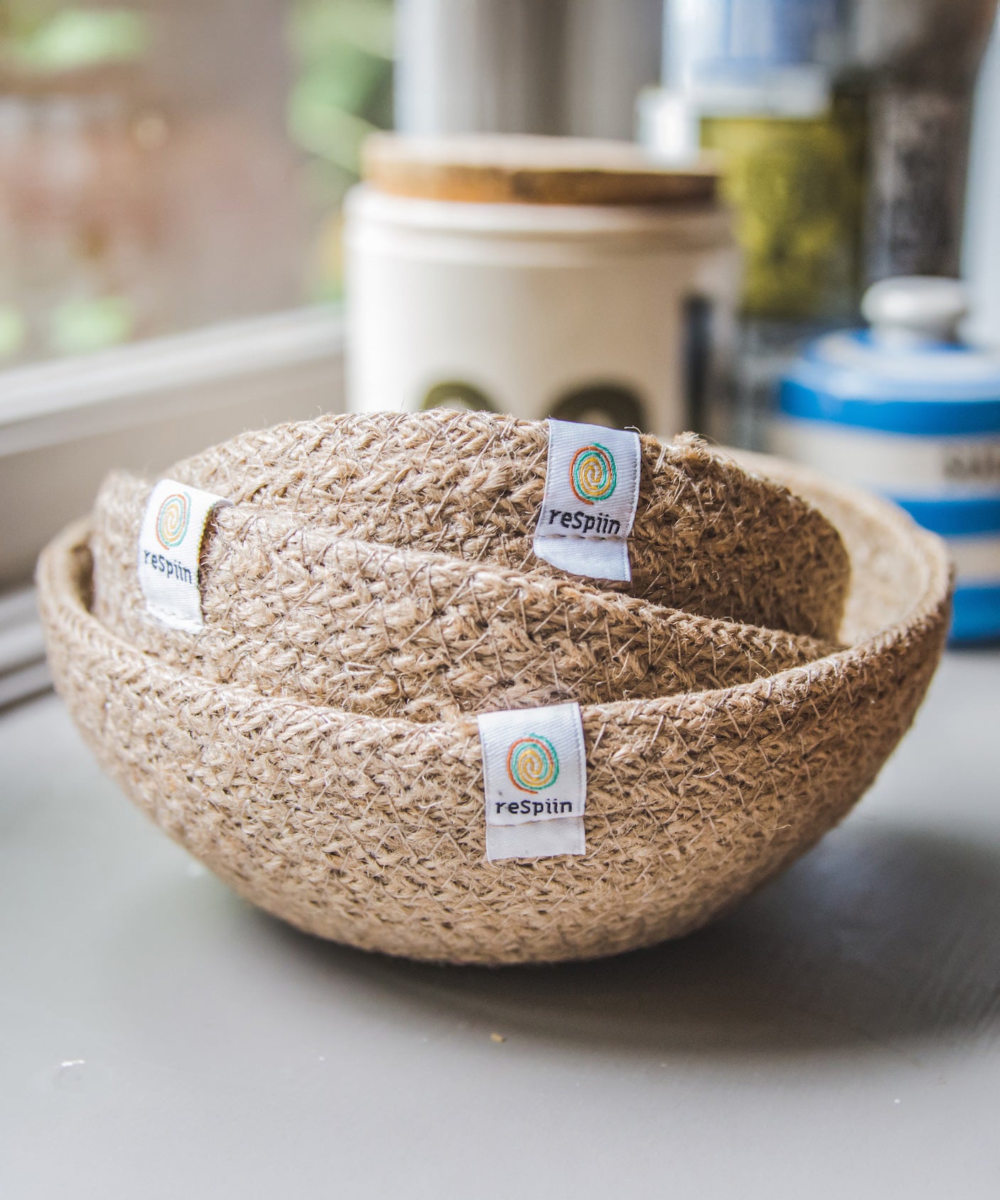 A set of three natural ReSpiin Jute Mini Bowl Set shown nestled inside each other on a window sill