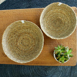 Large and medium Respiin seagrass woven natural bowls on a table on a tan & black placemat and a plant