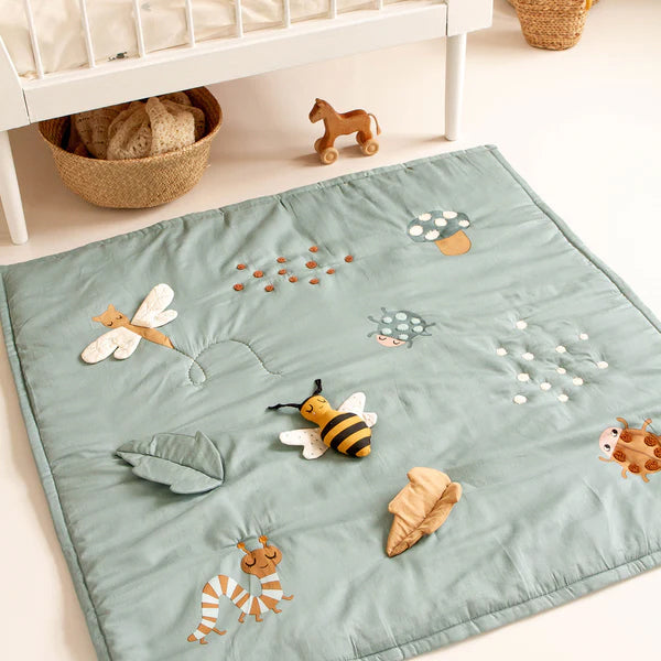 Roommate Baby Bugs Activity Blanket in a Sea Grey colour pictured on the floor in front of a crib