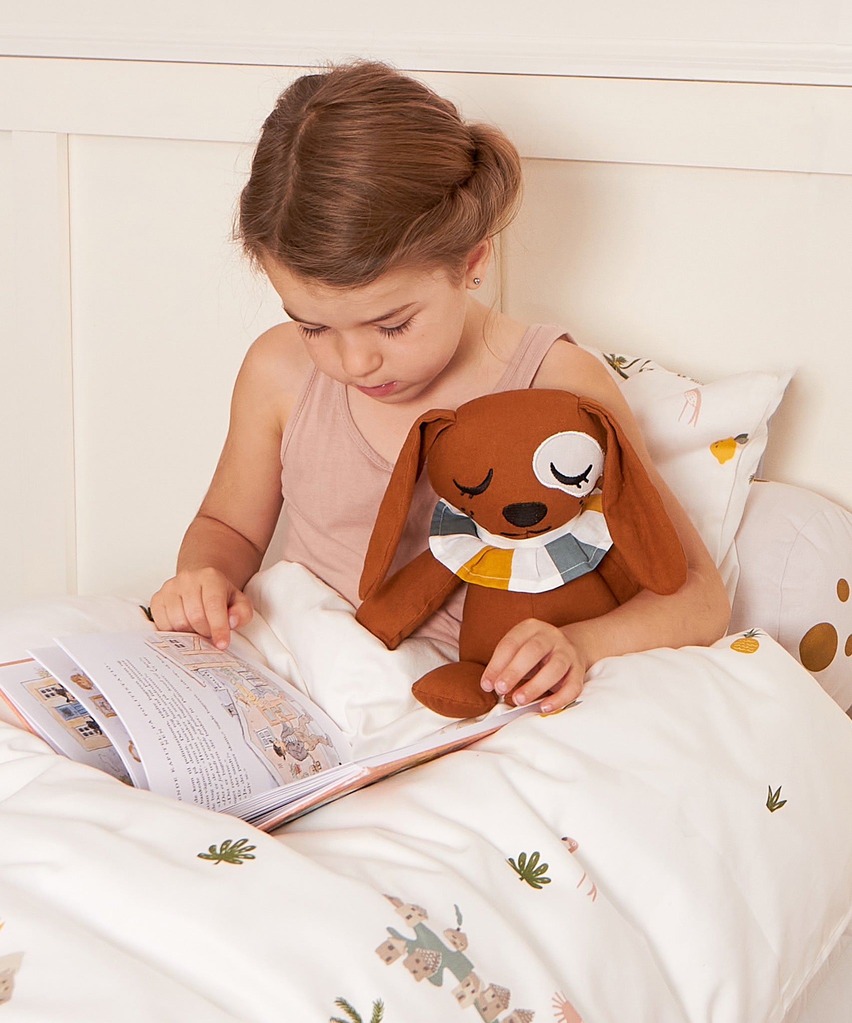 A child holding the Roommate Duke The Dog Canvas Doll whilst reading in bed. 