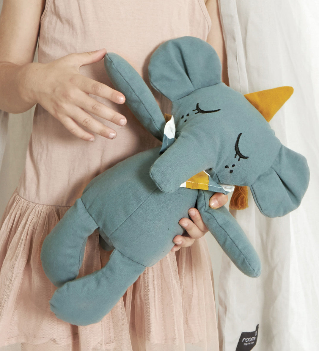 A close up of a child holding onto a Roommate Eddy The Elephant Canvas Doll.