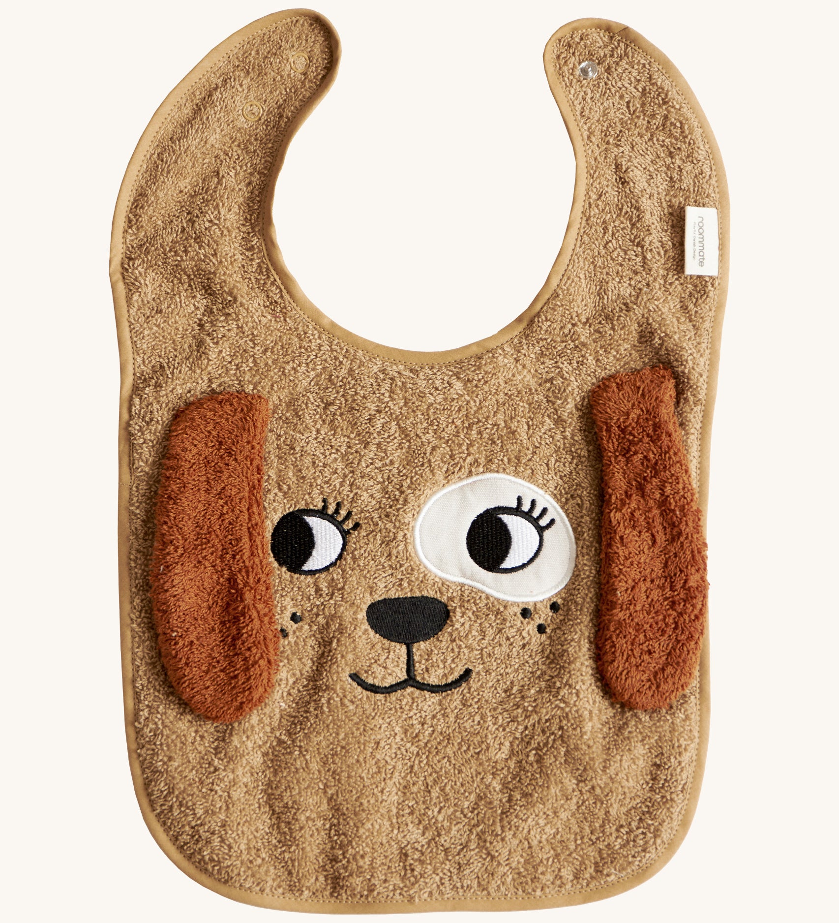 The Roommate Dog Baby Bib with an embroidered puppy face with floppy 3D ears. Cream background.