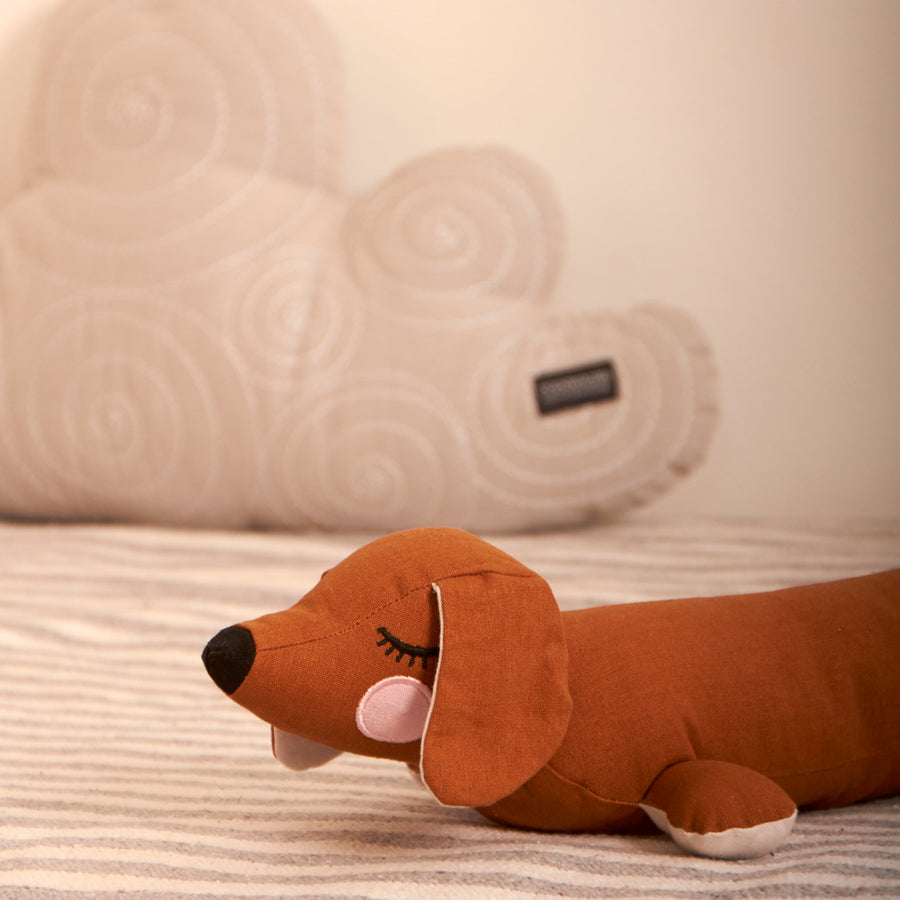 Close up of the Roommate organic cotton children's brown dog cushion on a striped carpet in front of a cloud cushion