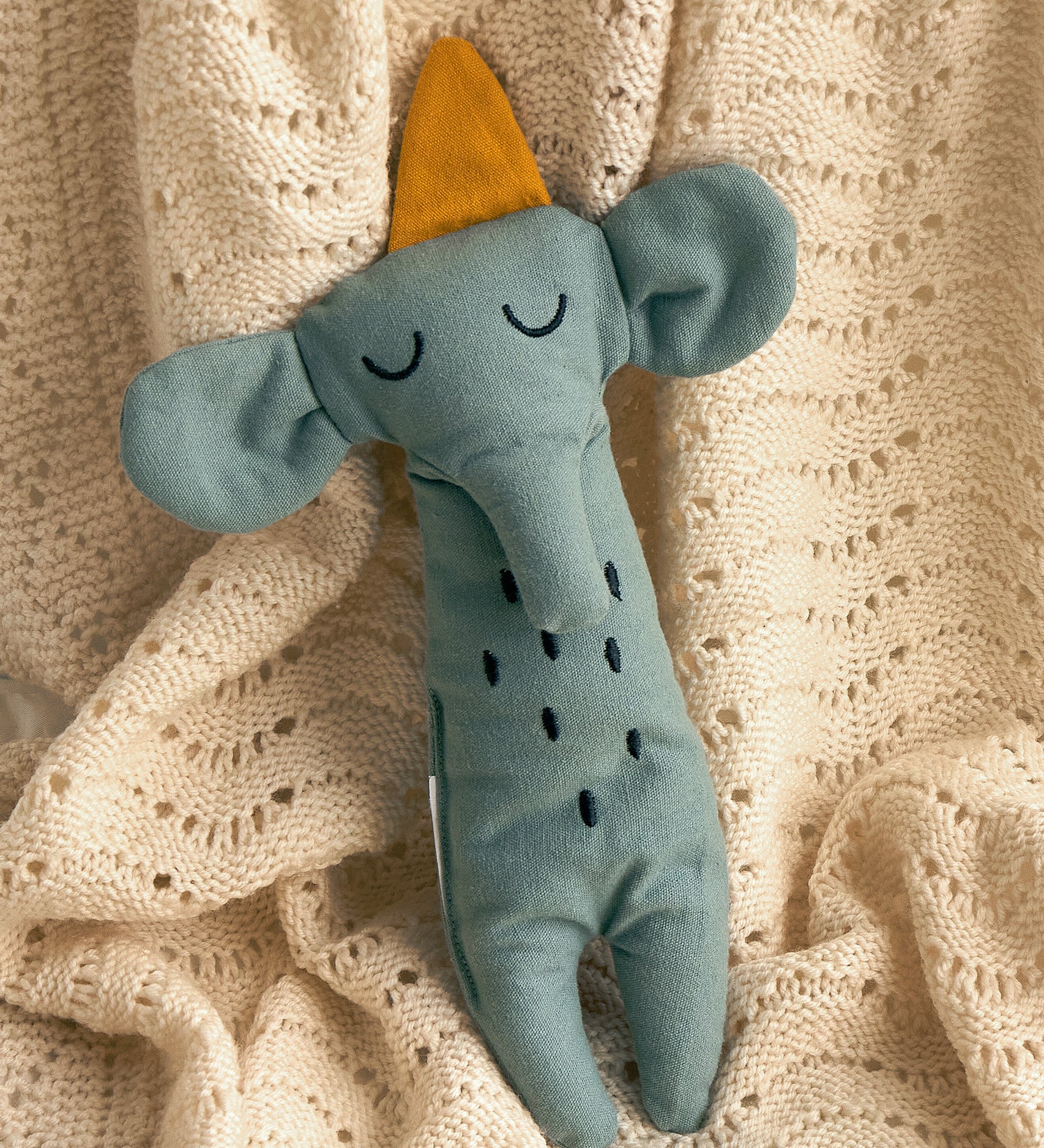 A Roommate Elephant Rag Doll on a cream coloured knitted blanket. 