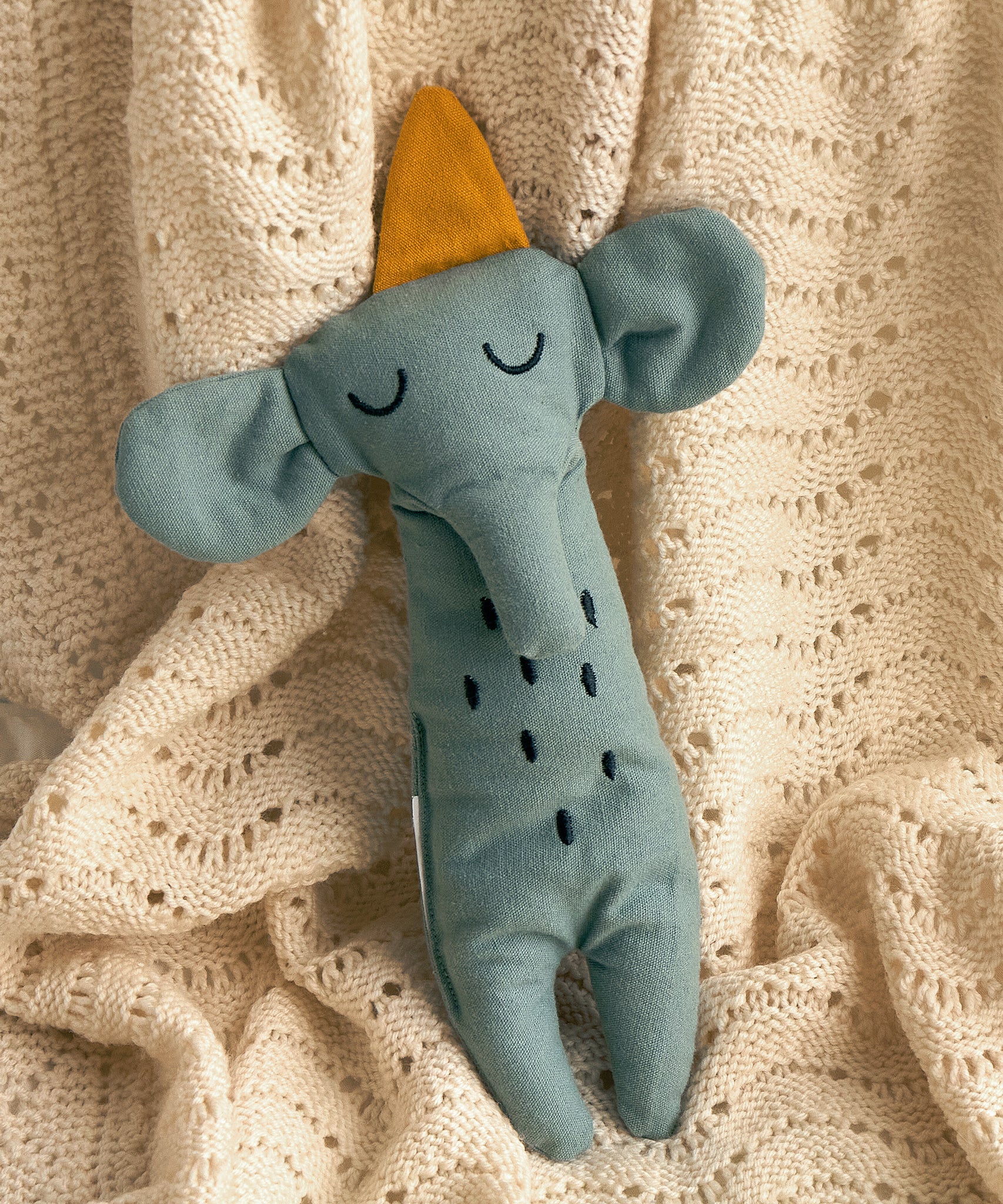 A Roommate Elephant Rag Doll on a cream coloured knitted blanket. 