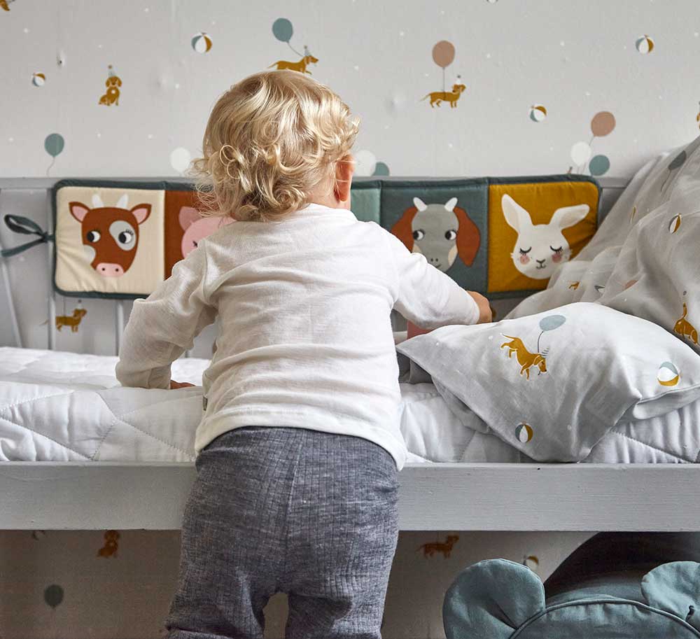 A child standing in front of a bed with the Roommate Country Life Fabric Book tied to the side.