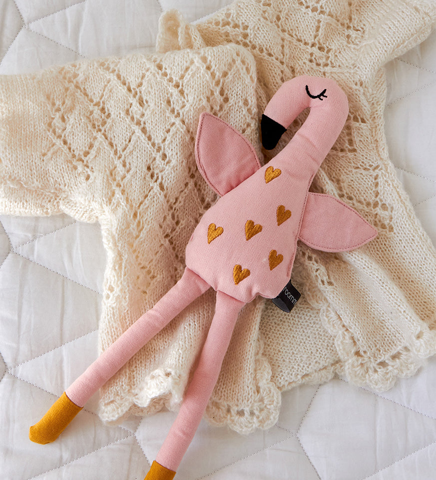 A Roommate Flamingo Rag Doll placed on a cream coloured knitted cardigan.