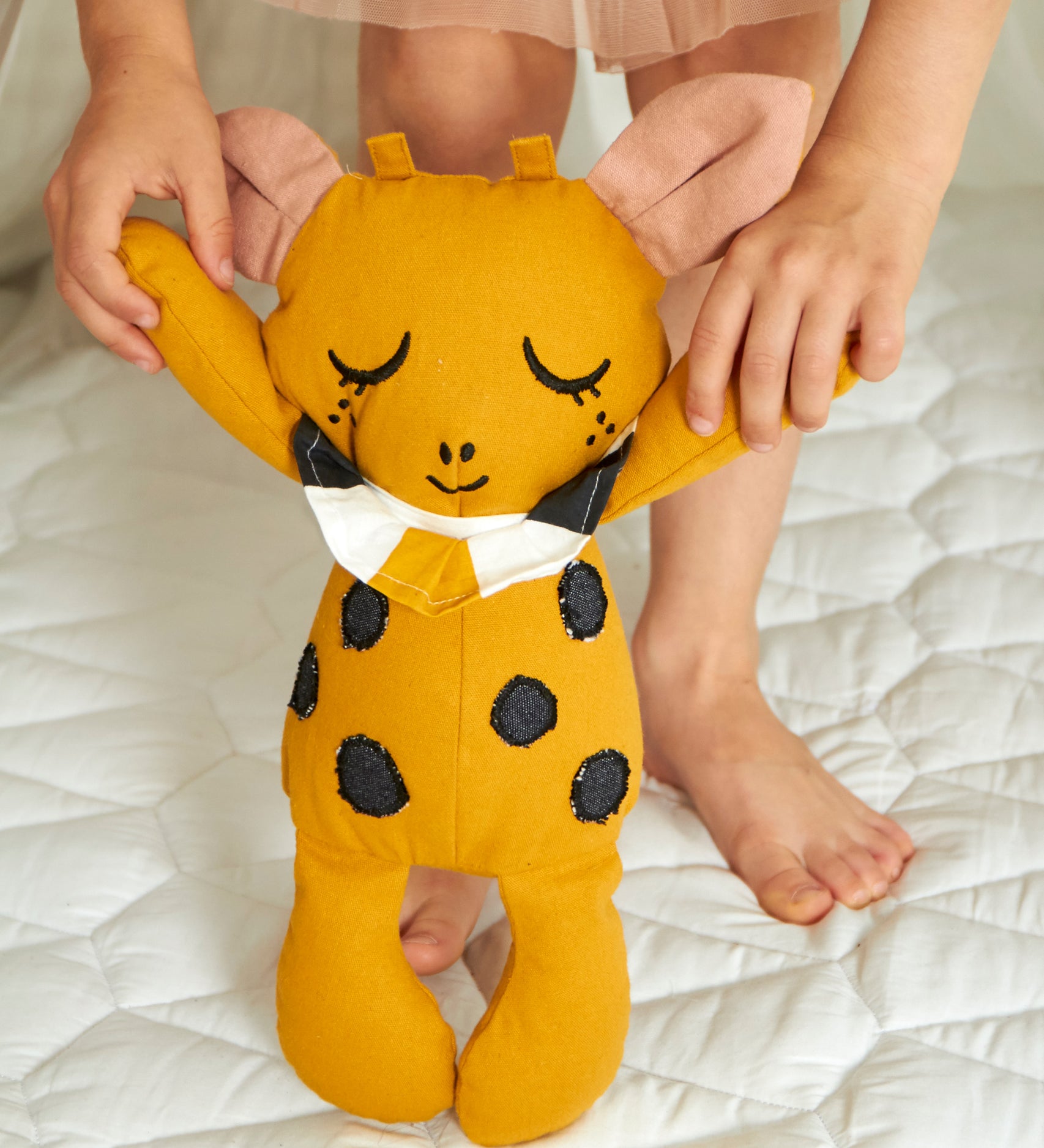 A child holding the Roommate Canvas Doll Goldy The Giraffe up in a standing position by it's arms. 
