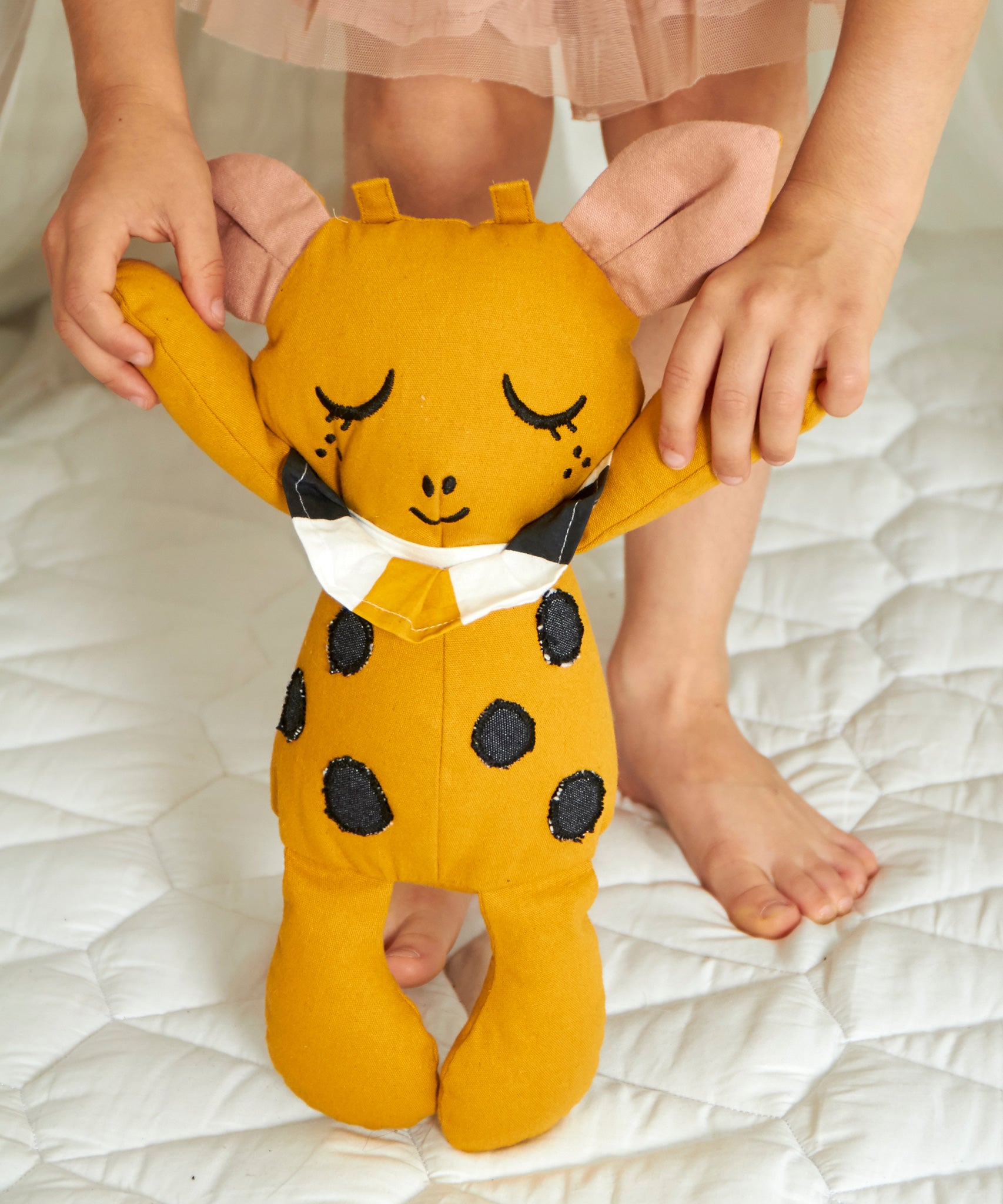 A child holding the Roommate Canvas Doll Goldy The Giraffe up in a standing position by it's arms. 
