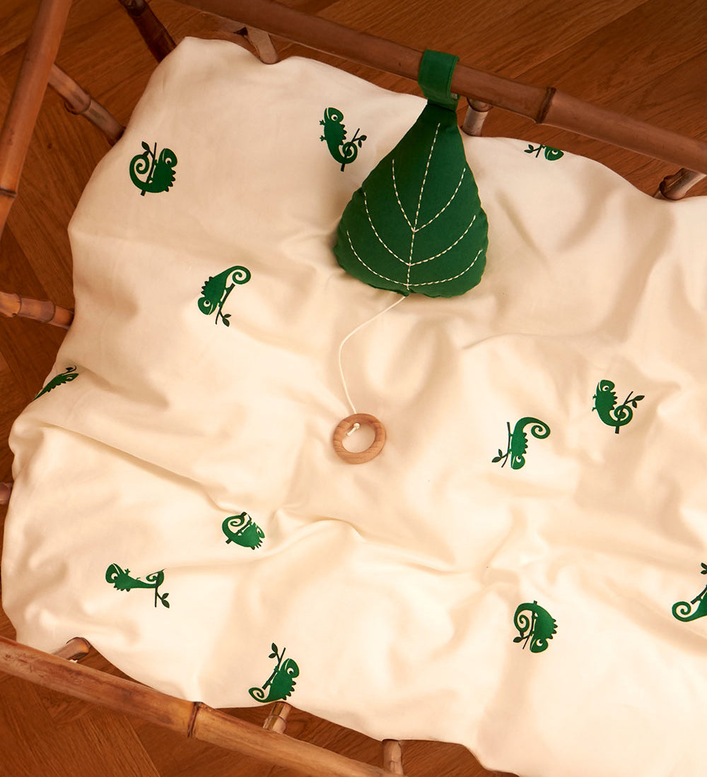 The Roommate Leaf Lullaby Music Mobile is attached to the inside of a crib, and is resting on a Roommate bed cover