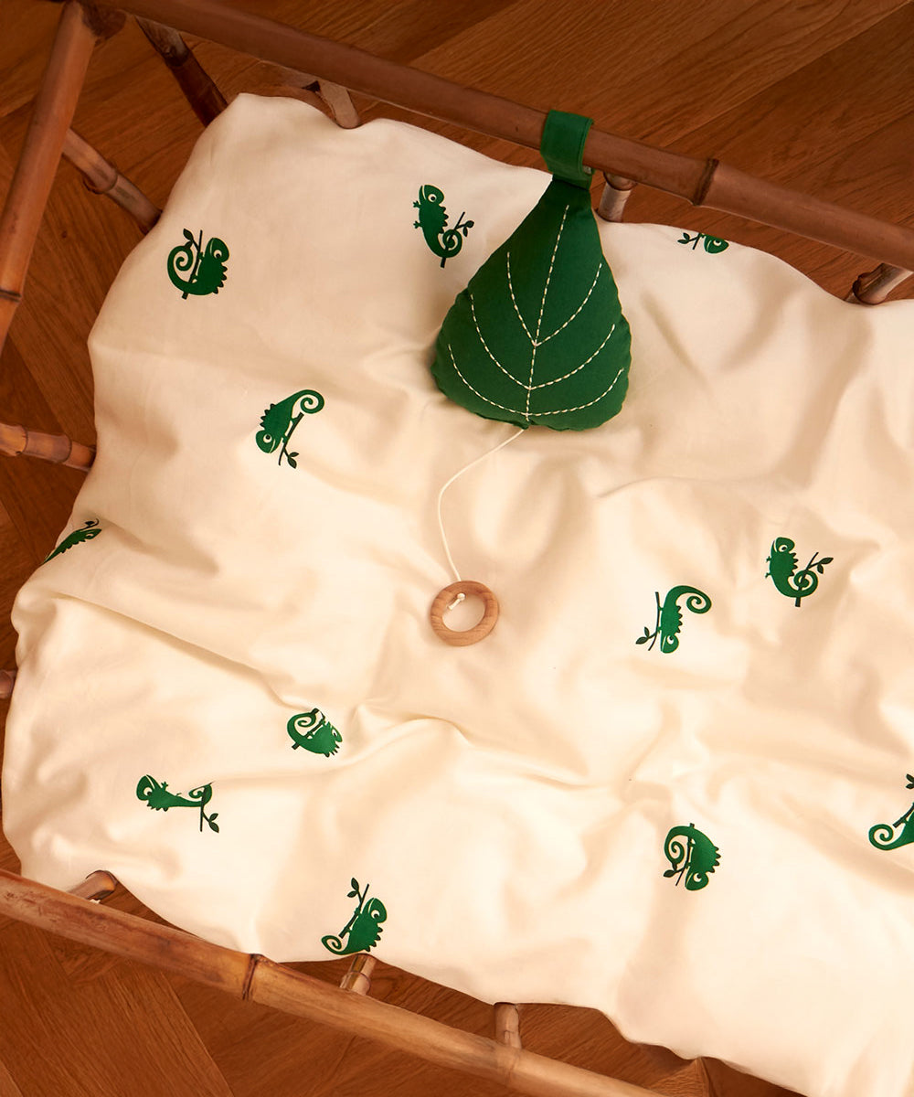 The Roommate Leaf Lullaby Music Mobile is attached to the inside of a crib, and is resting on a Roommate bed cover