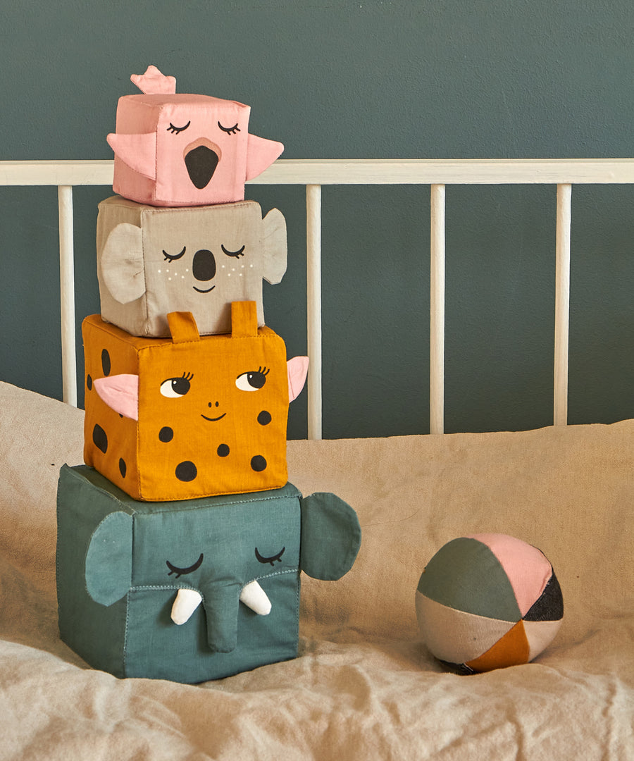 The Roommate Jungle Life Stacking Blocks placed on a bed next to a fabric ball. 