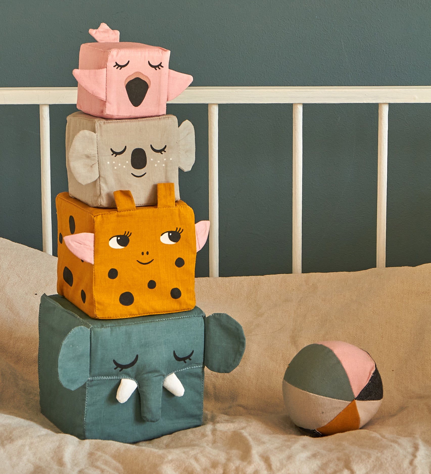 The Roommate Jungle Life Stacking Blocks placed on a bed next to a fabric ball. 