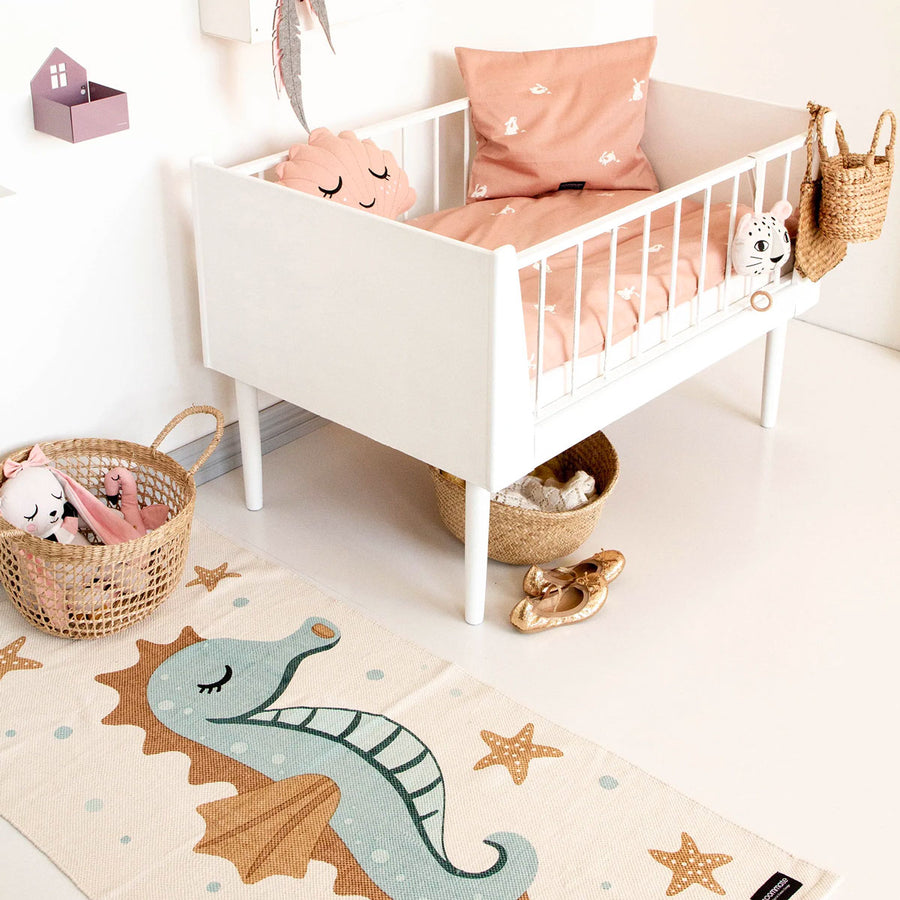 Roommate organic cotton floor mat with a seahorse print laid out on a white floor next to a child's bed