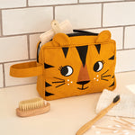 The Roommate organic cotton kids washbag, in a sunny yellow with an embroidered tiger design and 3D tiger ears. It is in a bathroom and filled with toiletries.