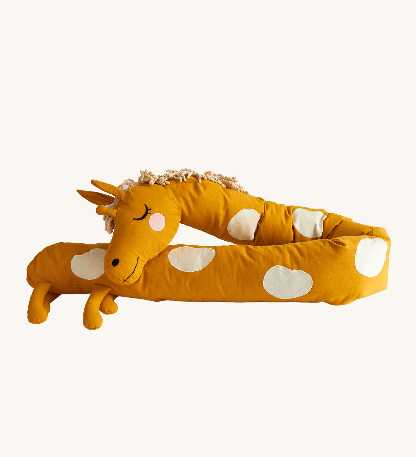 Roommate Long Organic Giraffe Cushion. A sleepy, smiling, long giraffe cushion in mustard yellow with cream spots, a curly mane and 4 small legs