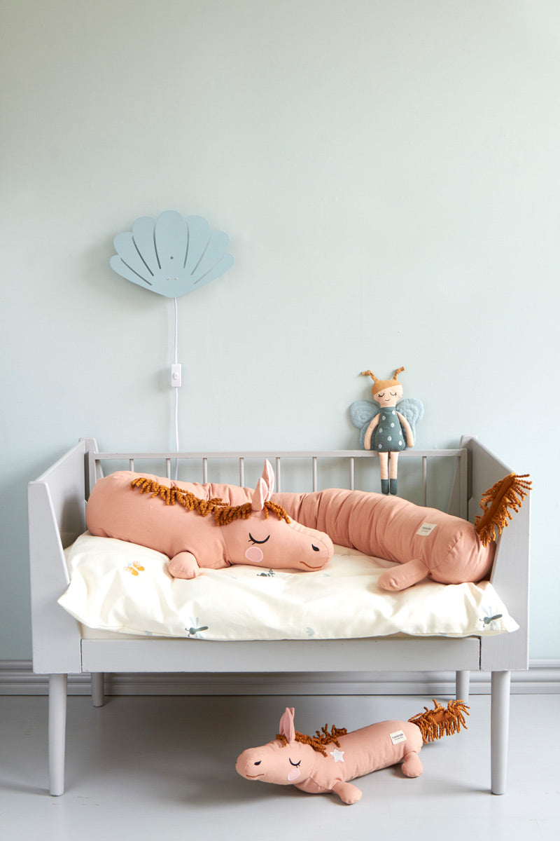 Roommate soft organic cotton long horse cushion laying on a childs bed