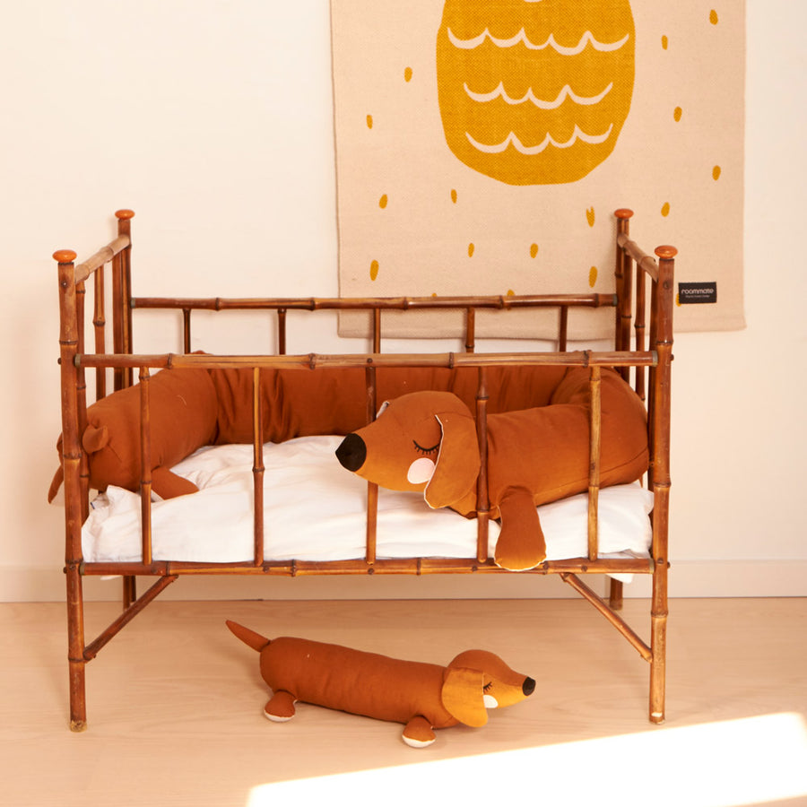 Roommate lazy puppy cushion and long dog cushion in a wooden cot in front of a white wall