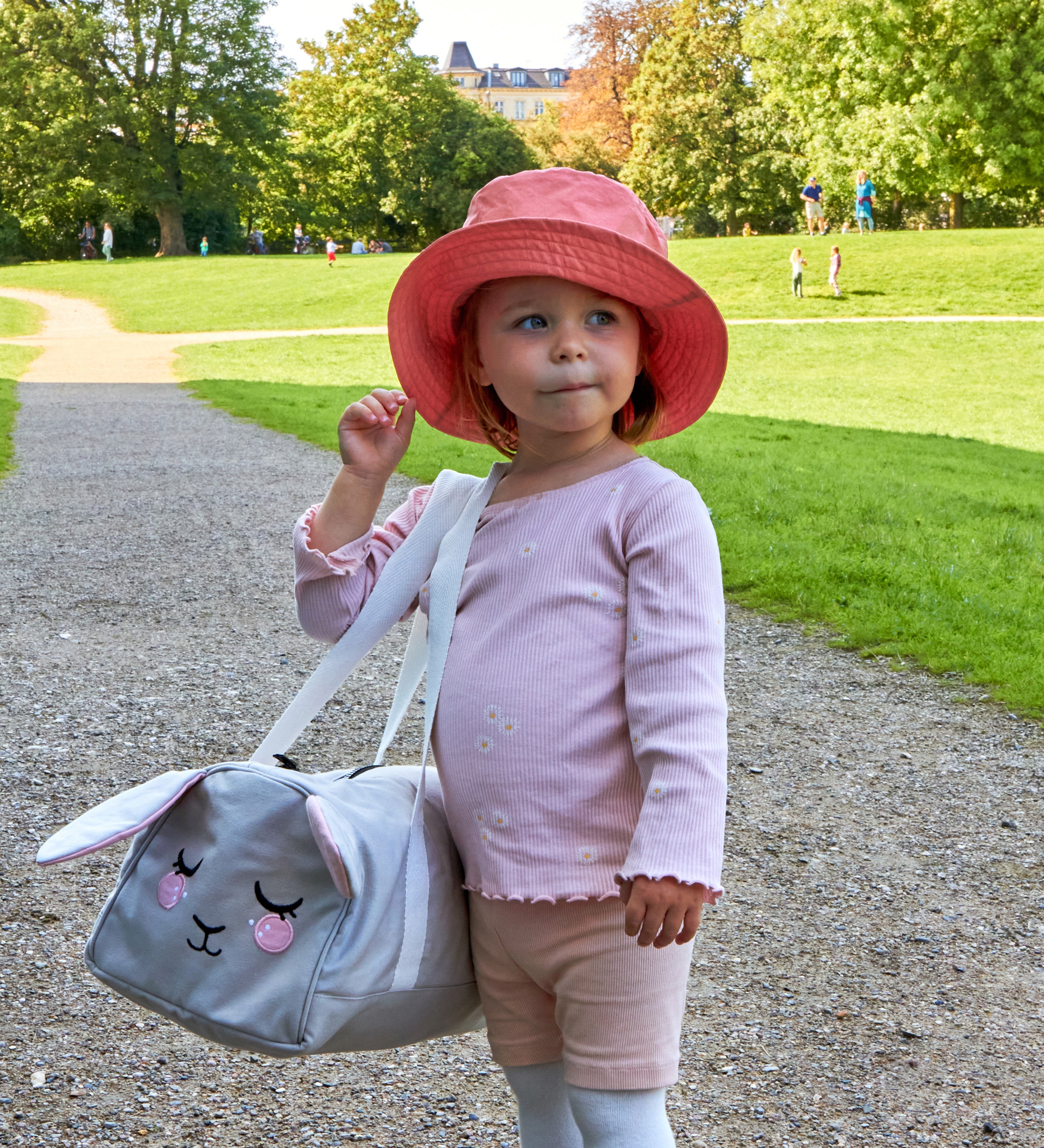 A child wearing a pink Roommate Mouse bucket hat in a park.